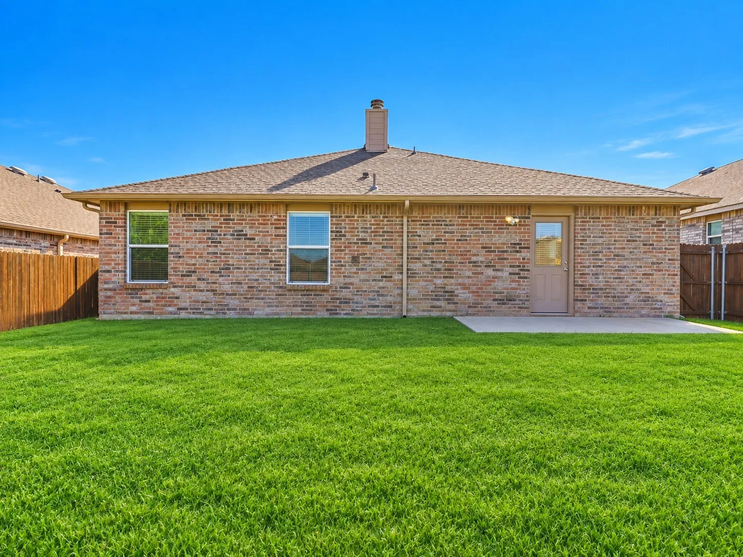 Expansive backyard featuring a lush lawn, a privacy fence, and an exterior patio with direct access to the brick-faced property