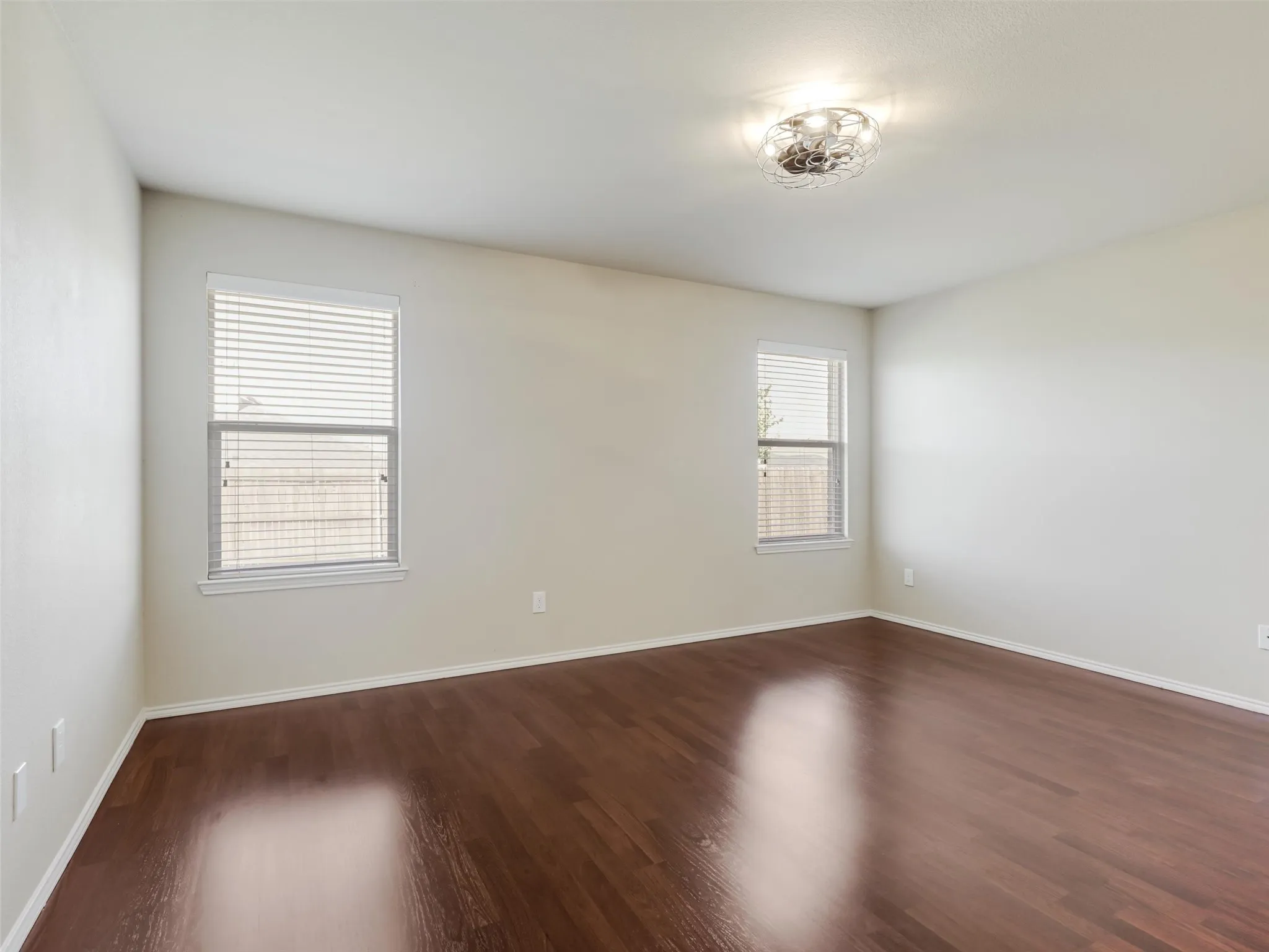 Spacious room featuring wood-finish flooring, two windows with blinds, and a modern ceiling light fixture