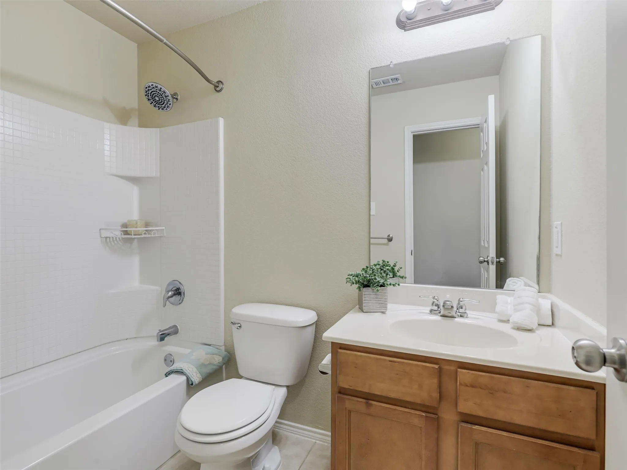 Tub-shower combination with white tile surround, wood-finish vanity with countertop, and integrated sink