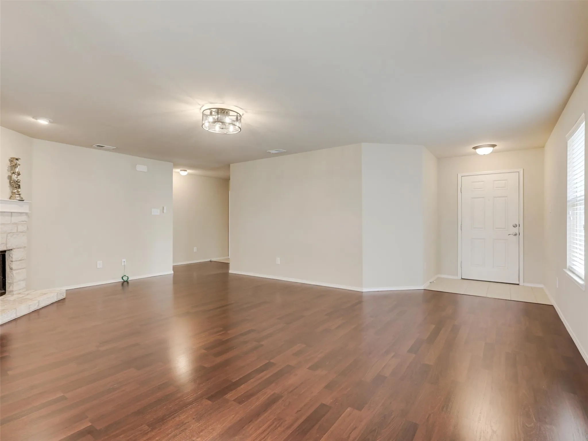 Expansive living area with rich wood-finish flooring, a stone-surround fireplace, and a contemporary flush-mount ceiling light
