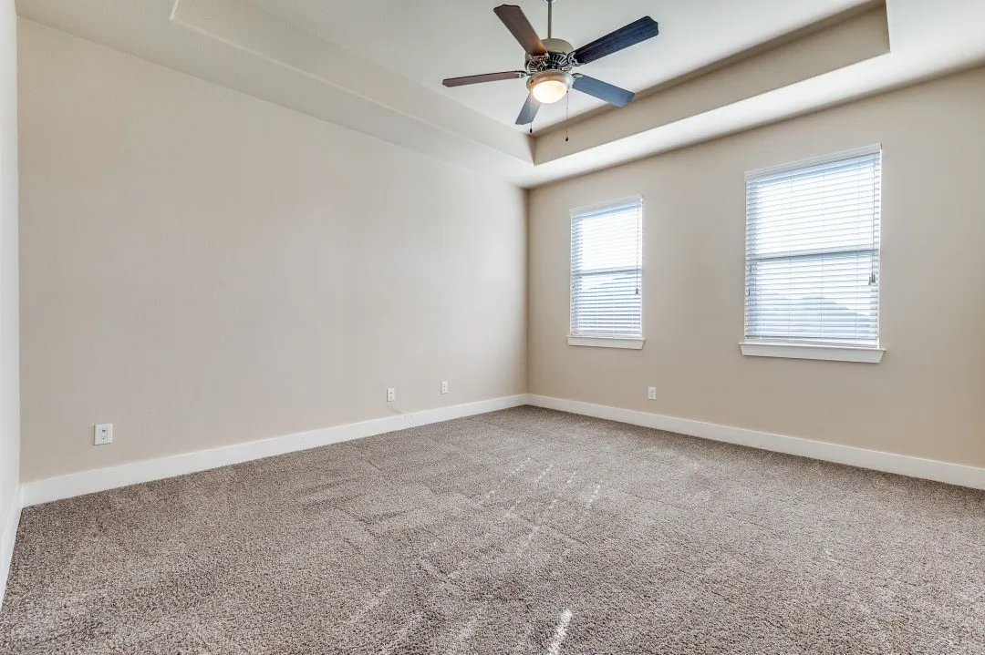 Tray ceiling with a ceiling fan, two windows with blinds, and carpeted flooring