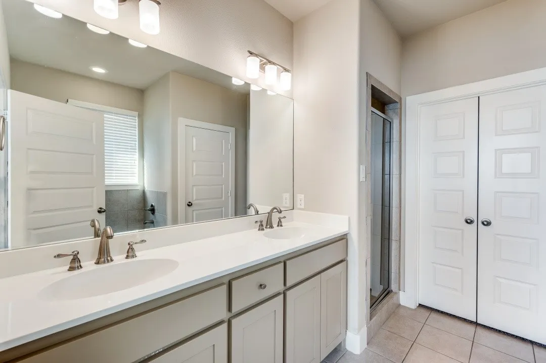 Dual undermount sinks, light-toned cabinetry, a spacious vanity mirror, brushed nickel fixtures, and tiled flooring