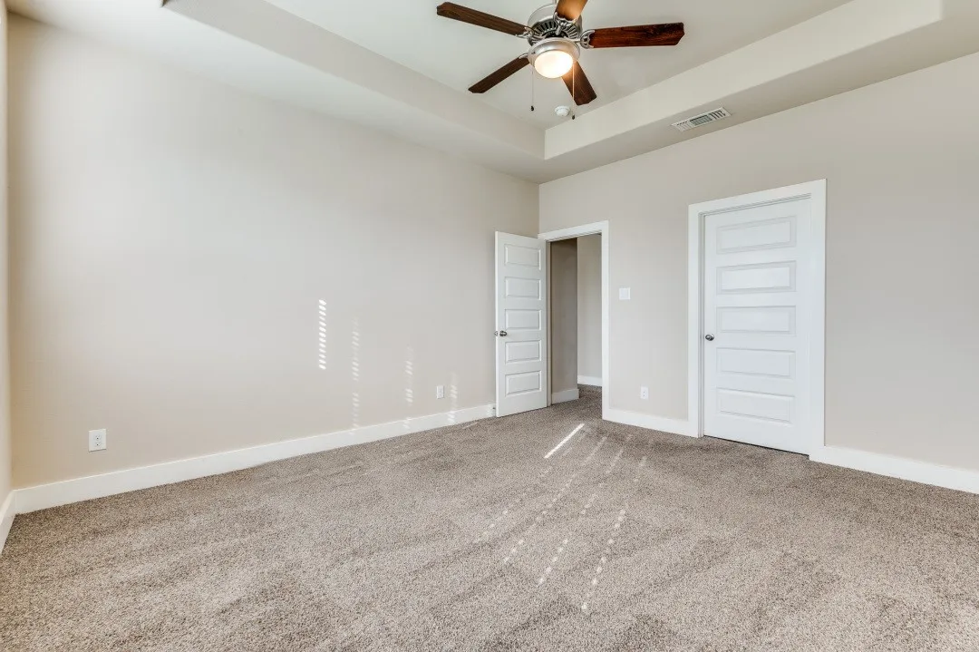 Tray ceiling with a ceiling fan, neutral carpeting, and white trim