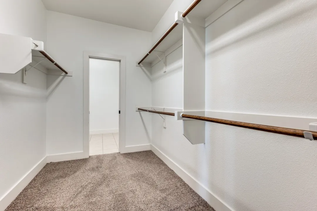 Walk-in closet featuring carpet flooring, crisp white walls, and multiple built-in shelving units with hanging rods
