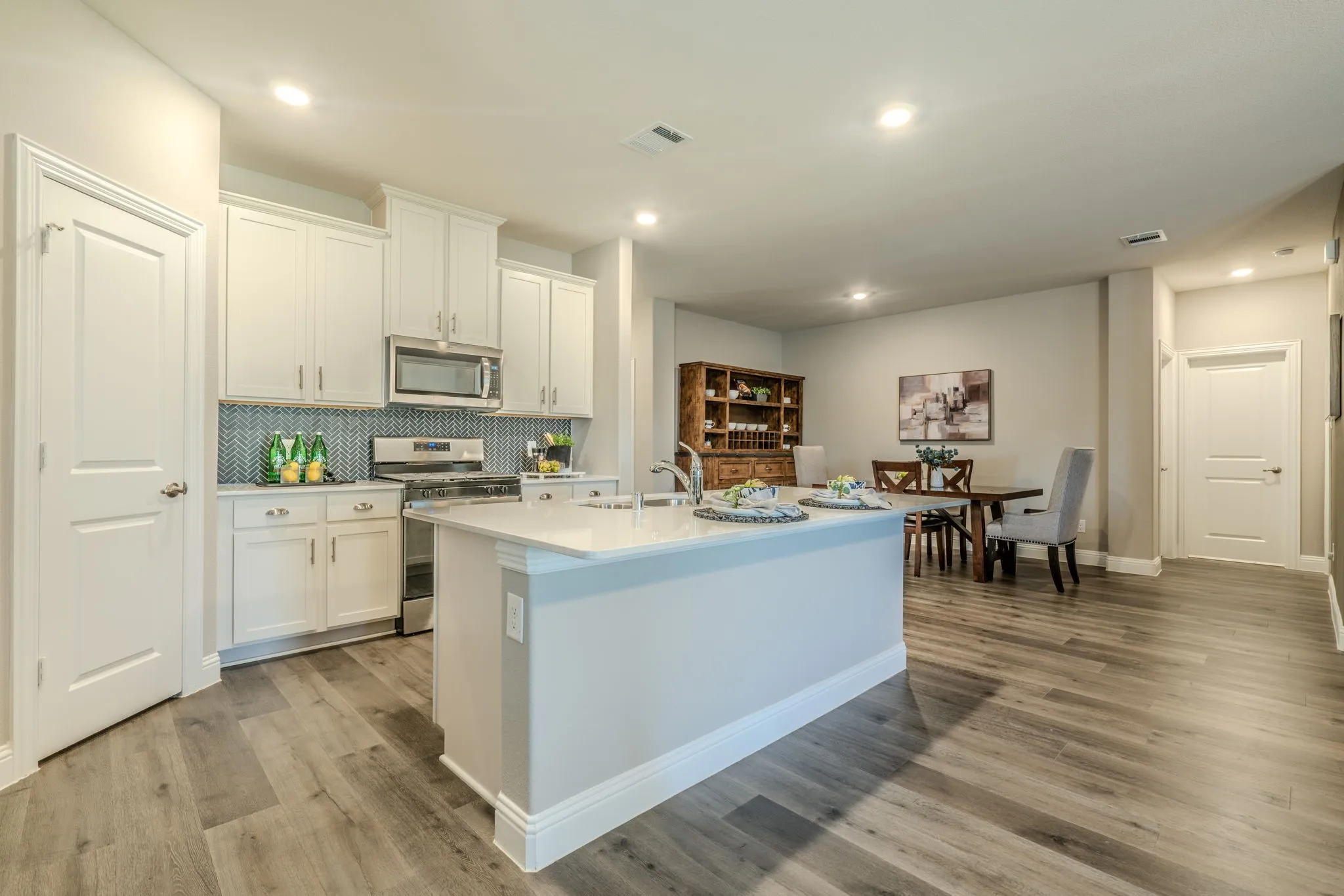 7329 Allium Court, Little Elm, TX 76227 - kitchen - Open-concept kitchen and living area featuring white cabinetry, stainless steel appliances, a light blue kitchen island with waterfall countertop, wood-finish flooring throughout, recessed lighting, and abundant counter workspace