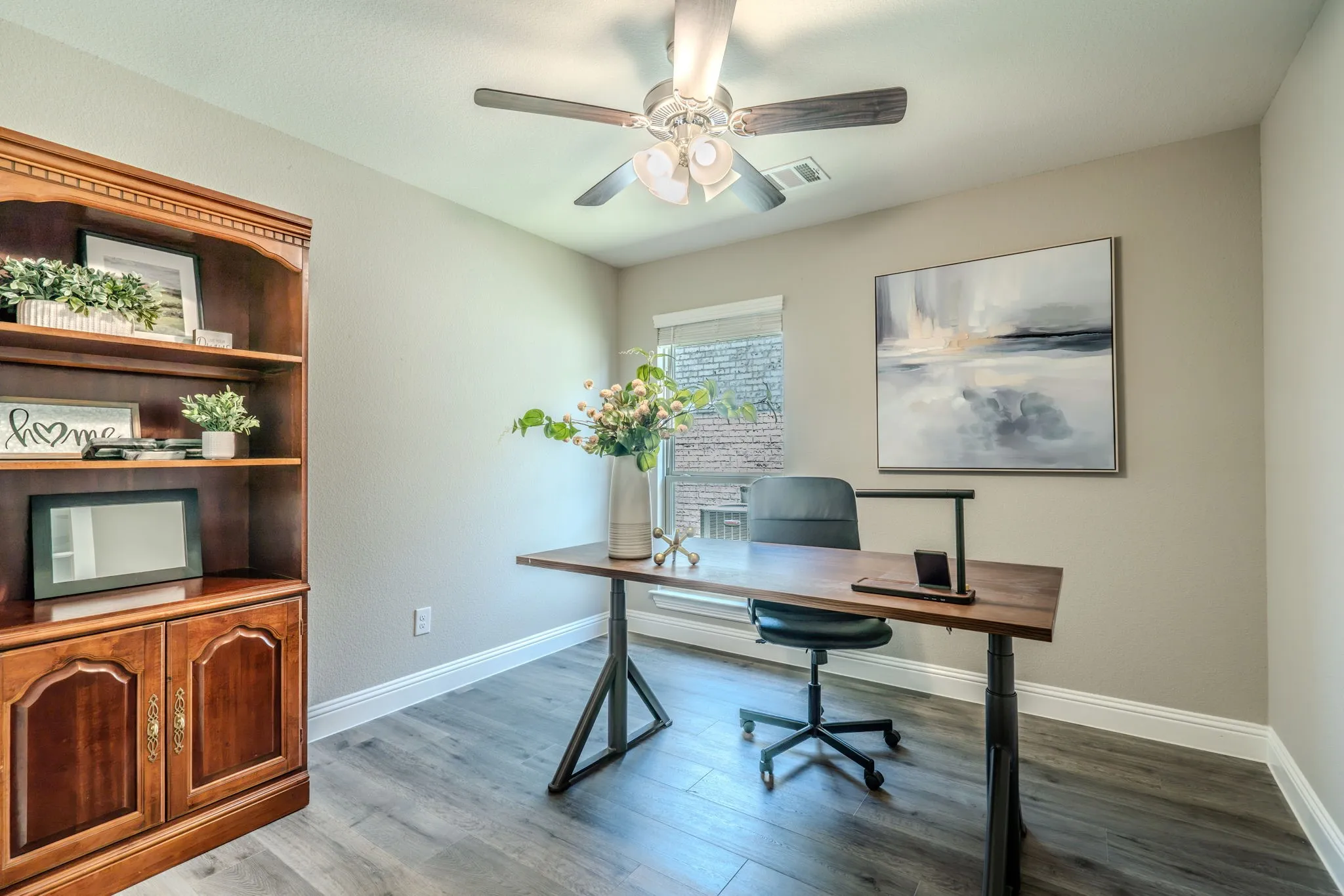 7329 Allium Court, Little Elm, TX 76227 - office - Dedicated home office featuring wood-finish flooring, built-in cabinetry with decorative shelving, a ceiling fan with integrated lighting, and ample natural light from a large window