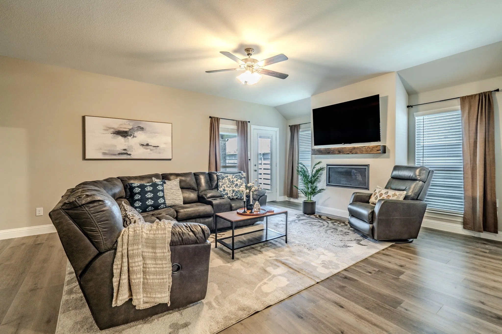 7329 Allium Court, Little Elm, TX 76227 - living room - Spacious living area featuring wood-finish flooring, a ceiling fan with integrated lighting, and a modern fireplace with a wood mantel