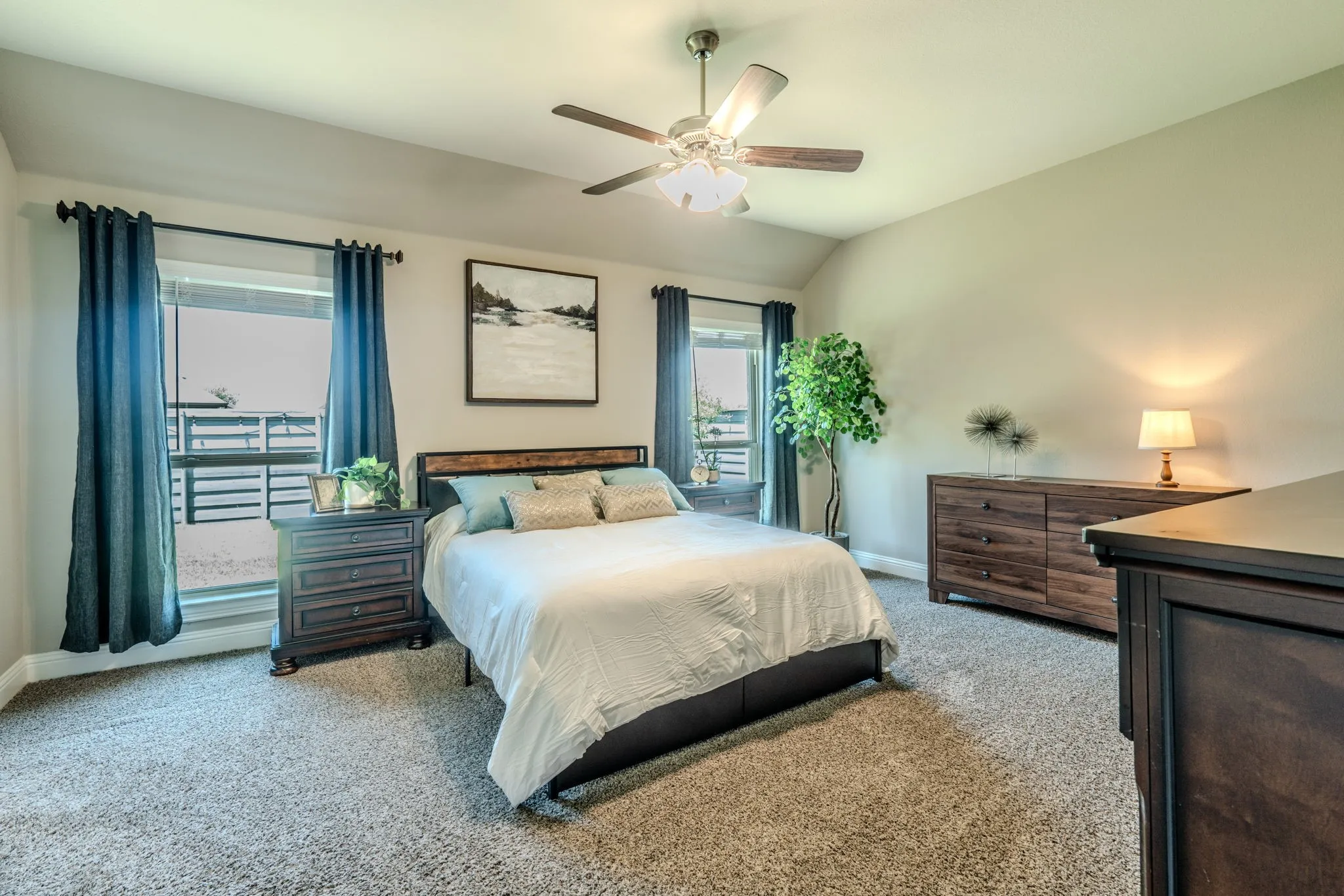 7329 Allium Court, Little Elm, TX 76227 - Primary Bedroom - Spacious primary bedroom featuring a wood-finish bed frame, dual glass-door access to a private balcony, ceiling fan with integrated lighting, carpet flooring, and coordinating wood-finish nightstands with task lighting