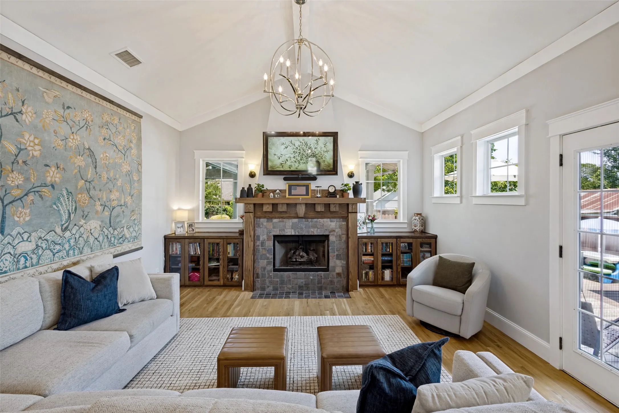Vaulted ceiling with an ornate chandelier, stone-faced fireplace with a wood mantle, built-in cabinetry, wood-finish flooring, and a glass-paned door