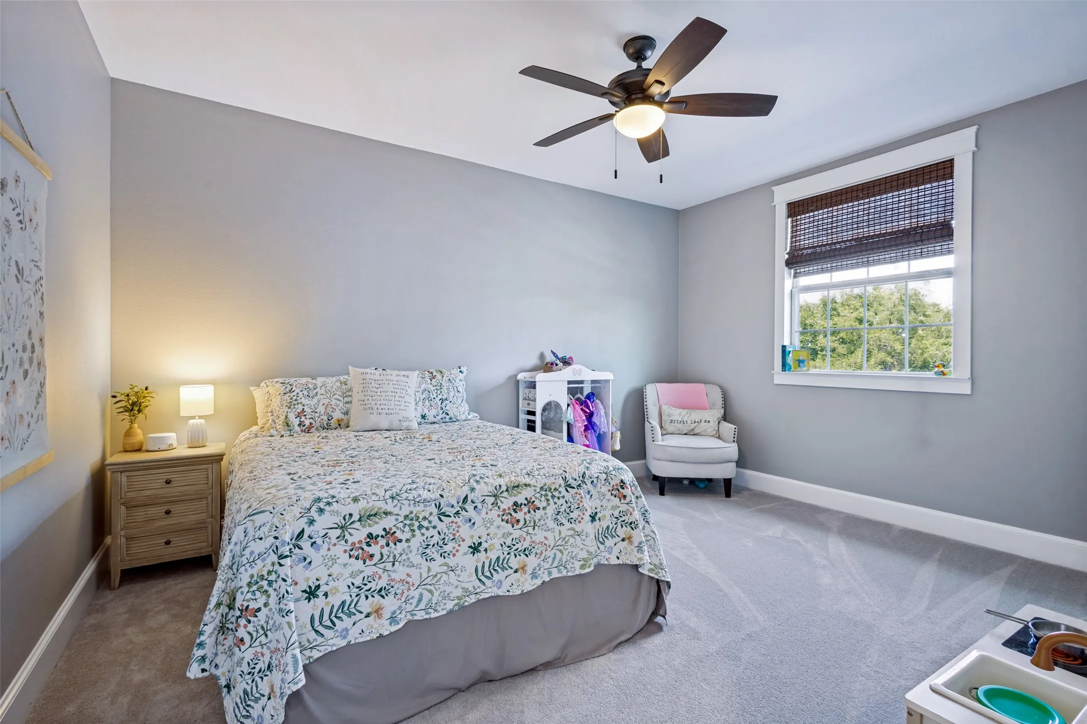 Carpeted flooring, a window with a woven shade, a ceiling fan with integrated lighting, and painted walls