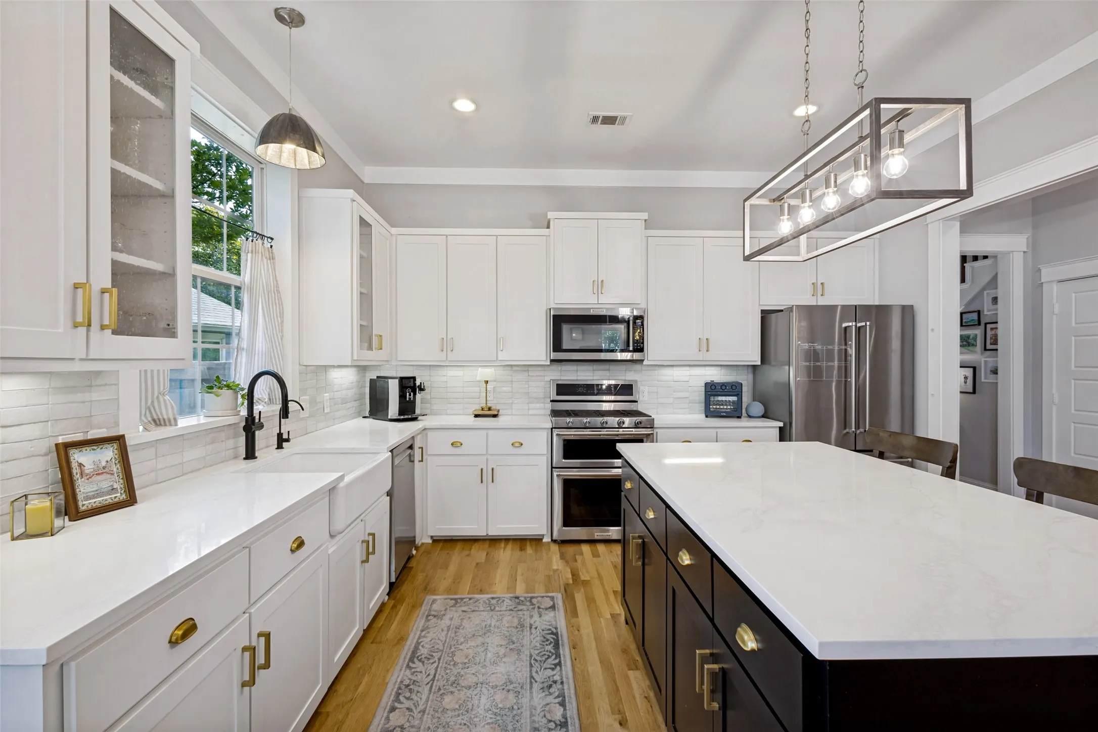 White cabinetry with brass hardware, wood-finish flooring, white subway tile backsplash, stainless steel appliances, and a central island with a white countertop