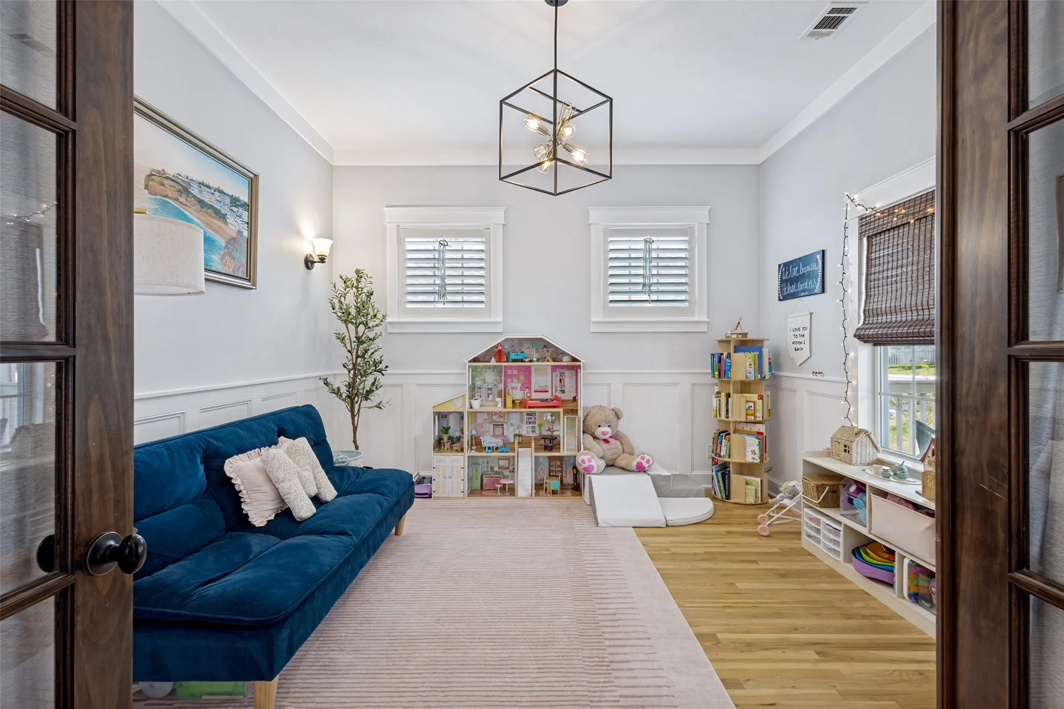 Wood-finish flooring, wainscoting, crown molding, built-in shelving, and a decorative ceiling fixture