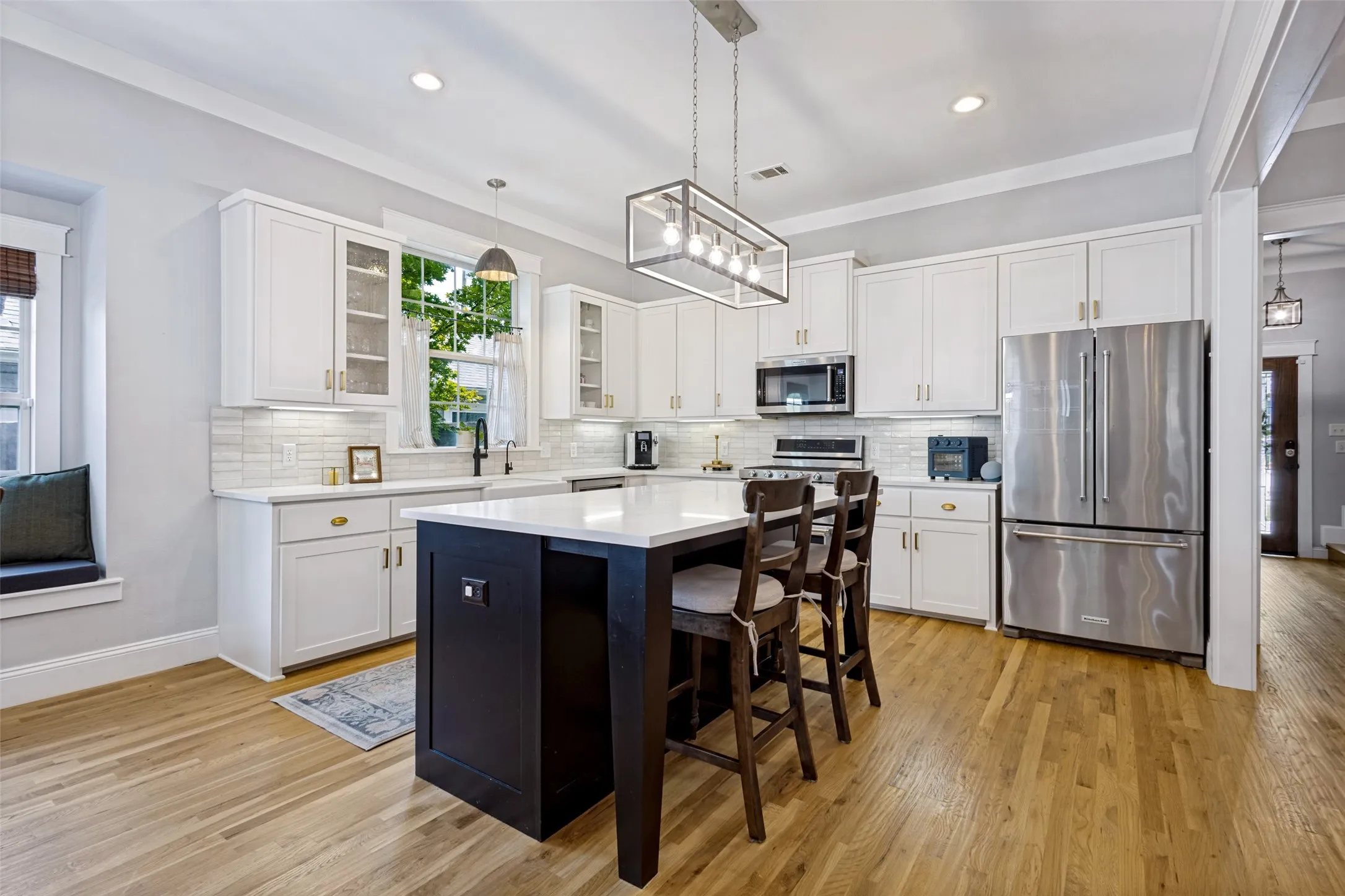 Bright kitchen featuring white cabinetry, a dark-toned island with seating, stainless steel appliances, and wood-finish flooring