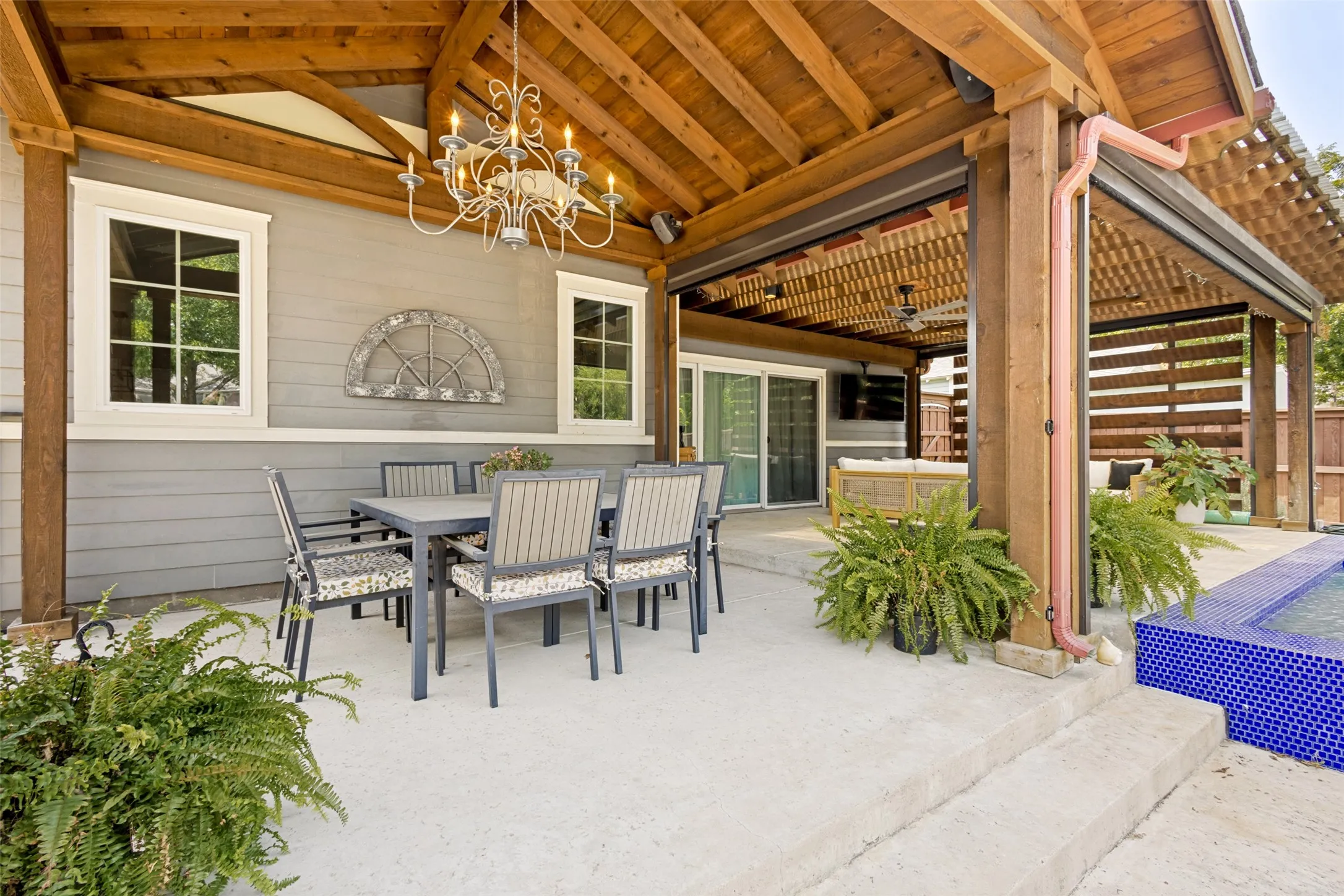 Expansive concrete patio with a vaulted wood-beam ceiling, custom outdoor lighting, and an integrated pool with blue tile