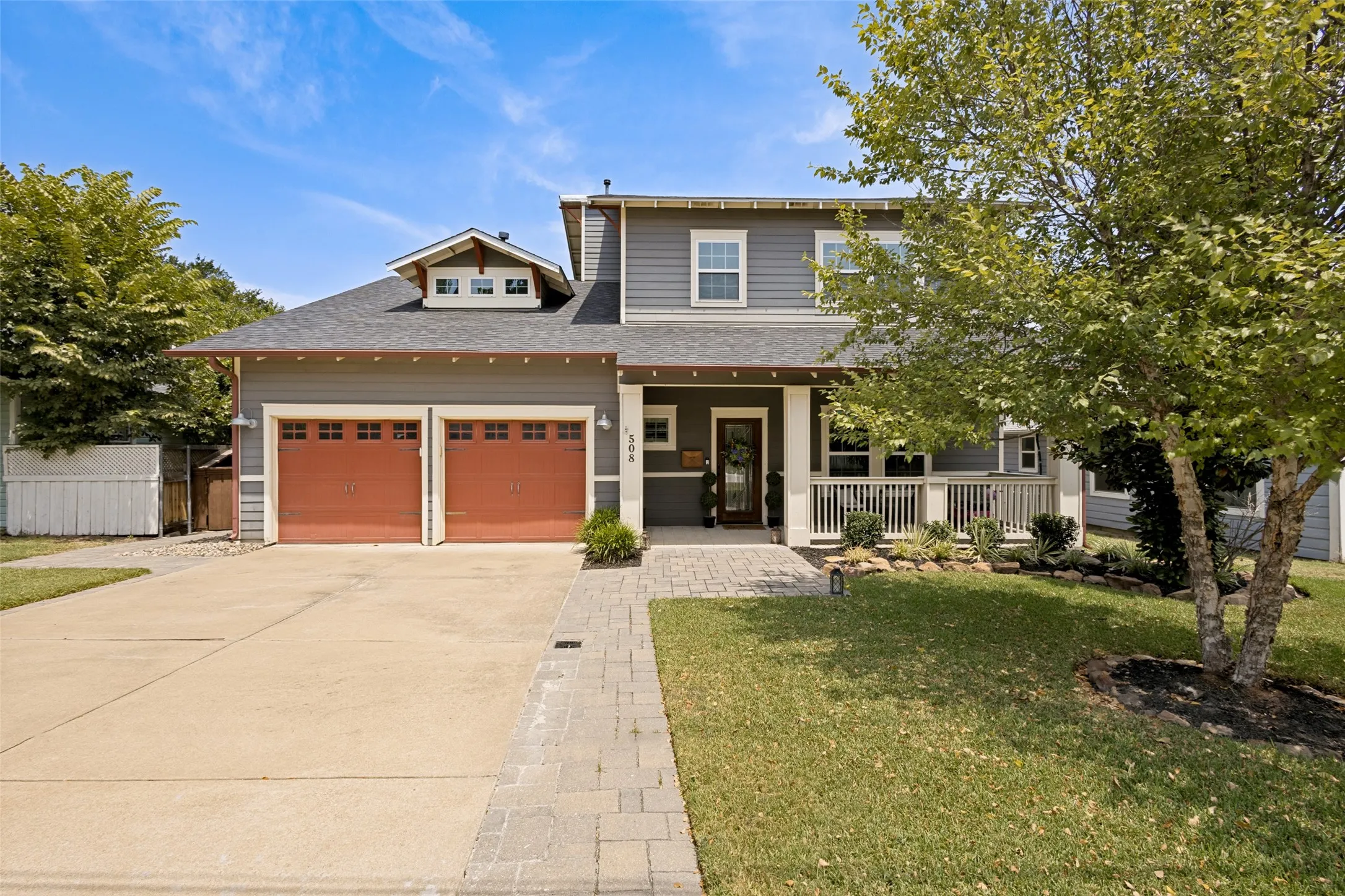 Craftsman-style exterior with gray siding, a covered front porch with white railings, a two-car garage with carriage-style doors, a concrete driveway, and a paver walkway