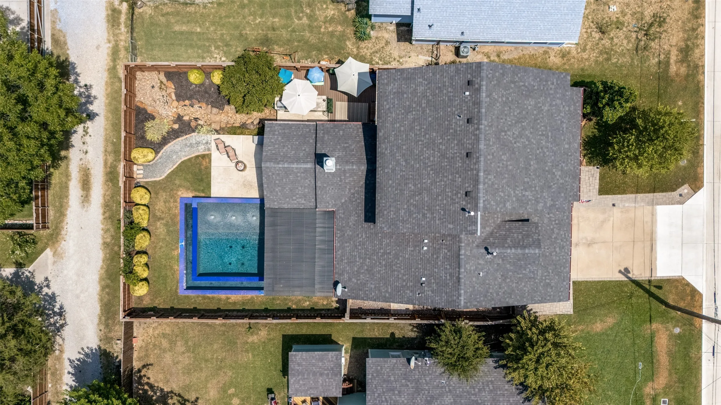 In-ground swimming pool, expansive paved patio, landscaped backyard, paved driveway, and perimeter fencing