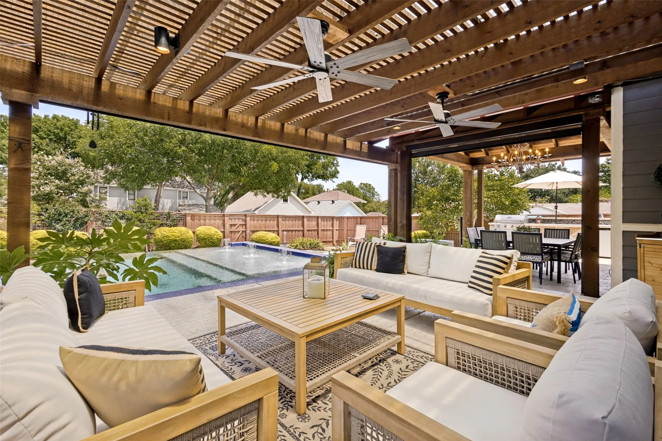 Expansive outdoor living area featuring a wooden pergola, ceiling fans, recessed lighting, and a built-in swimming pool with water features