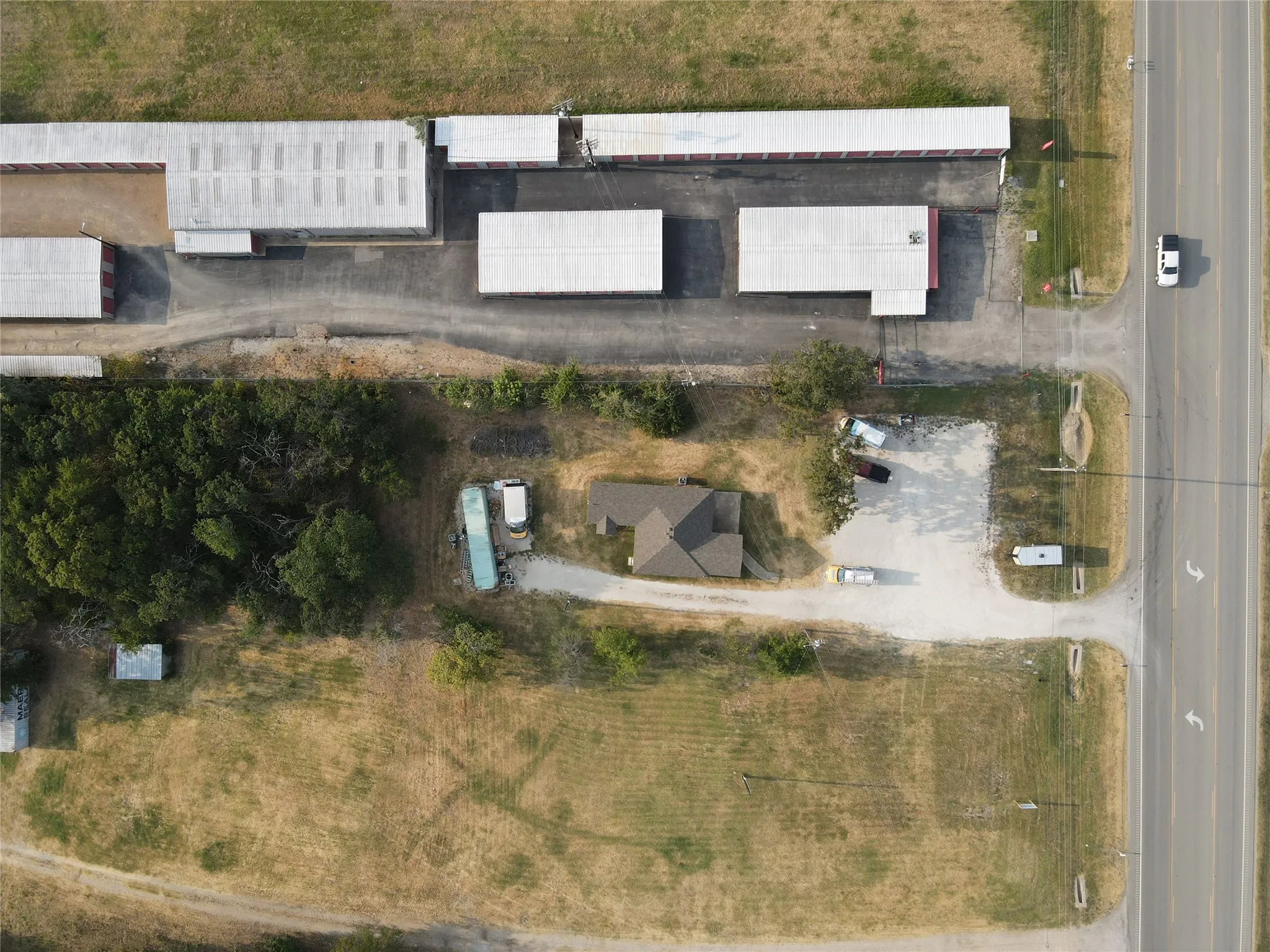 Aerial view of a commercial property featuring multiple storage buildings, a detached structure with a brown roof, paved road frontage, and a gravel lot