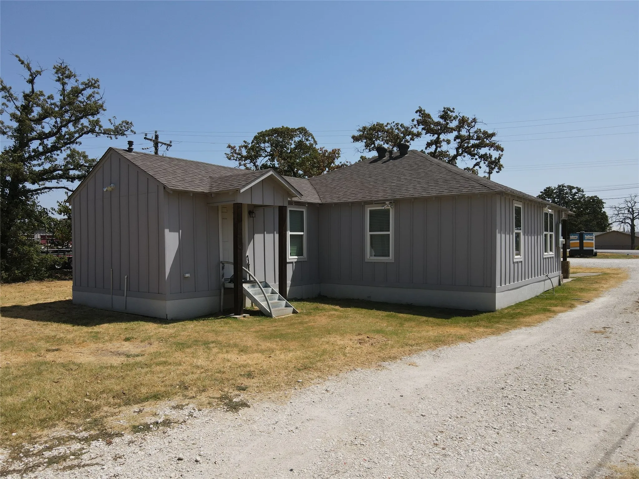 Light gray vertical siding exterior with a dark gray shingle roof, complemented by white trim windows and a covered entry with steps