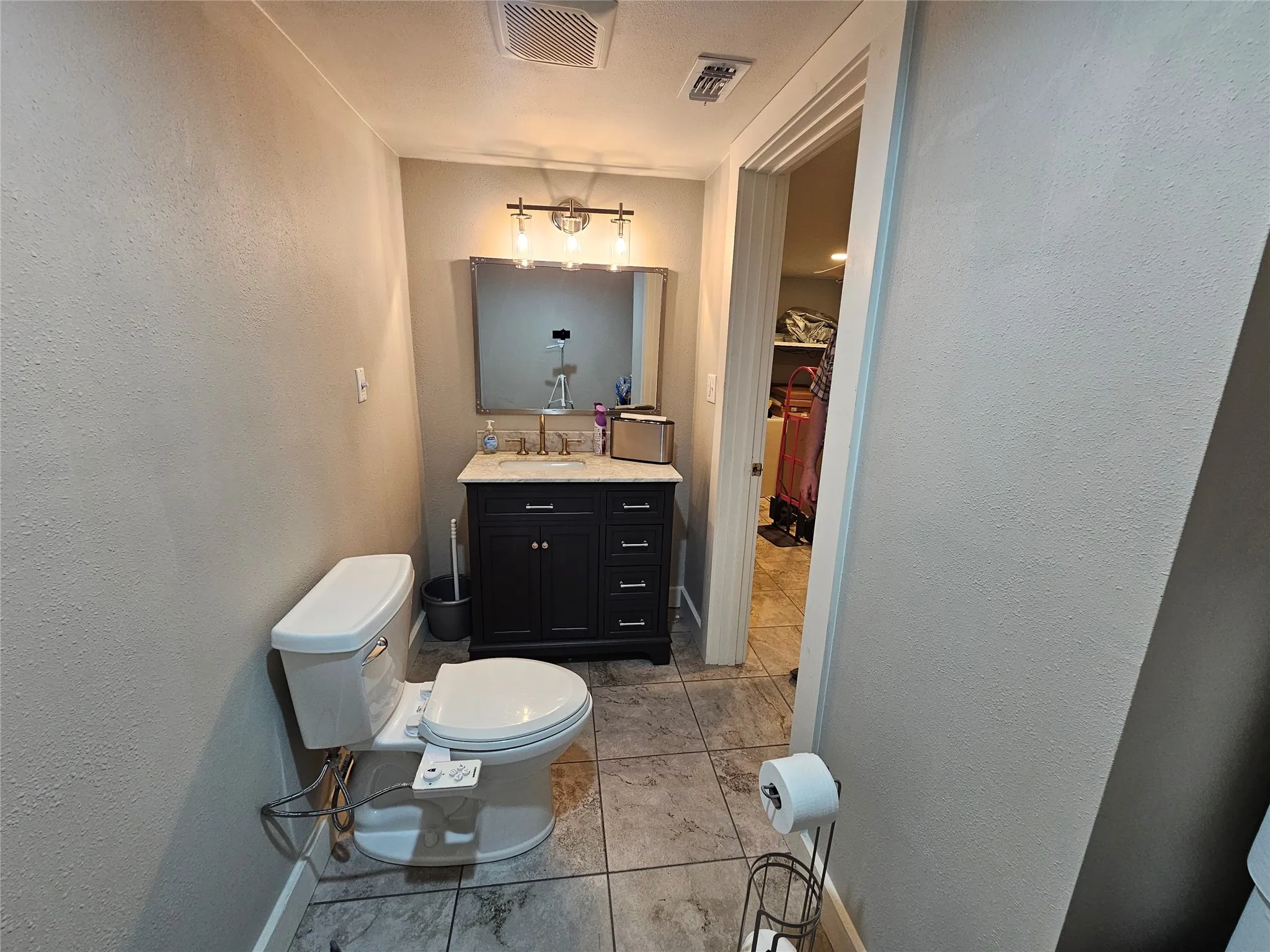 Bathroom featuring a dark wood-finish vanity with a rectangular mirror, a polished chrome light fixture with three glass shades, and neutral-toned wall paint