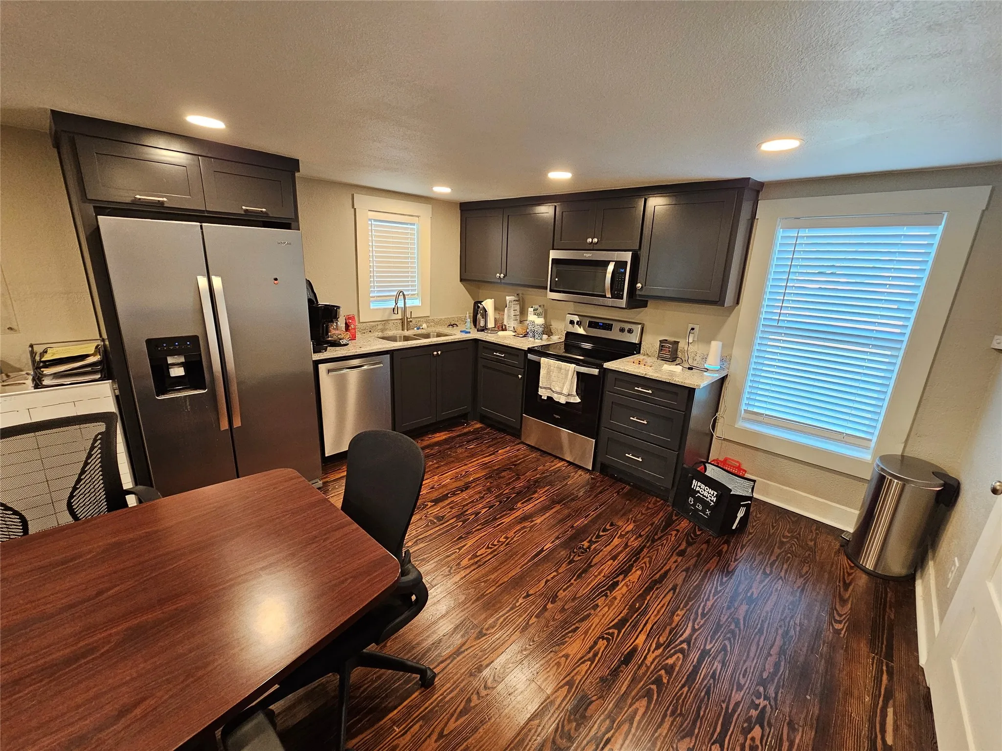 Modern kitchen and dining area featuring stainless steel appliances, including a side-by-side refrigerator and built-in microwave, dark cabinetry with ample storage, and a large wood-finish dining table