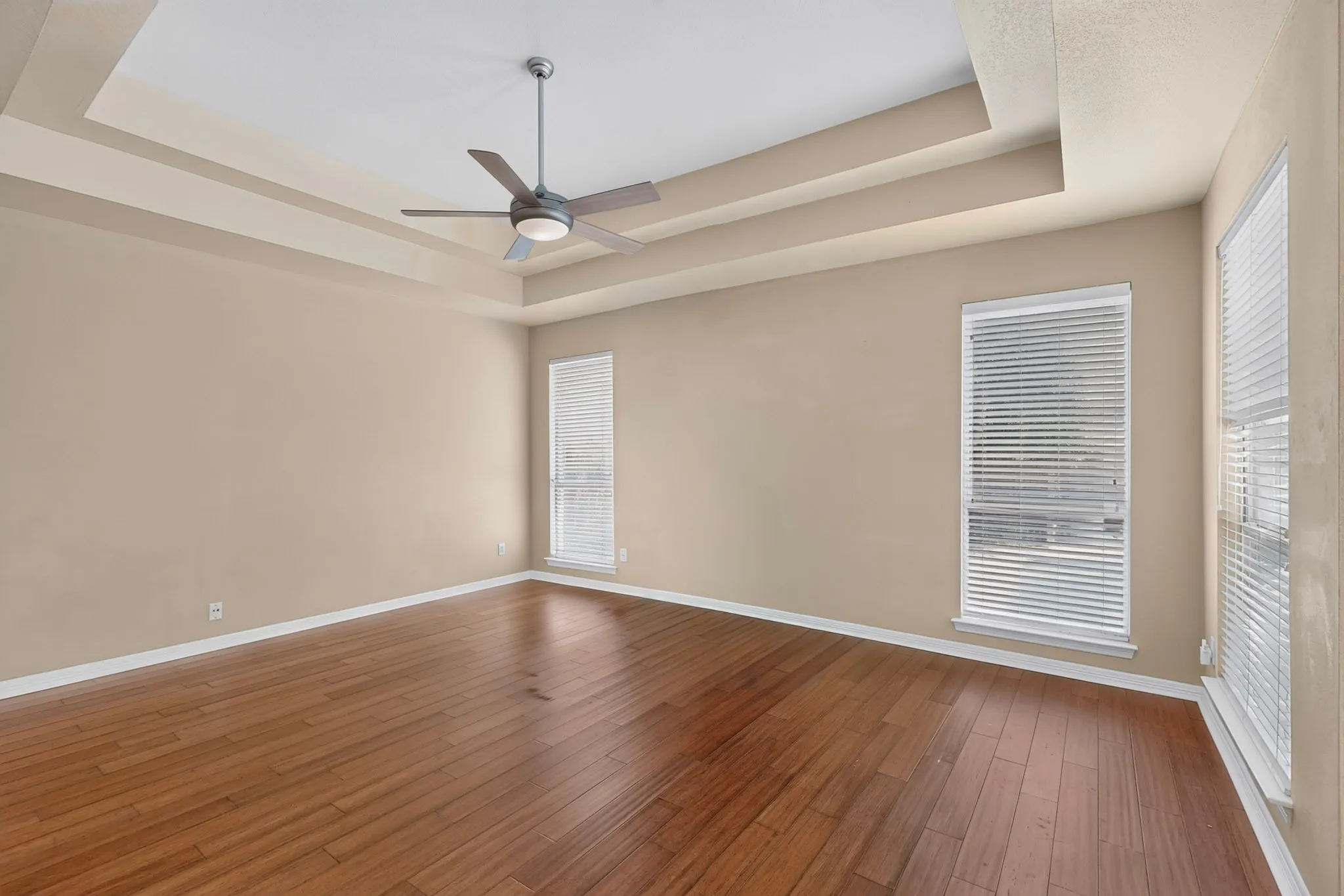 Tray ceiling with a ceiling fan, wood-finish flooring, and multiple windows with blinds