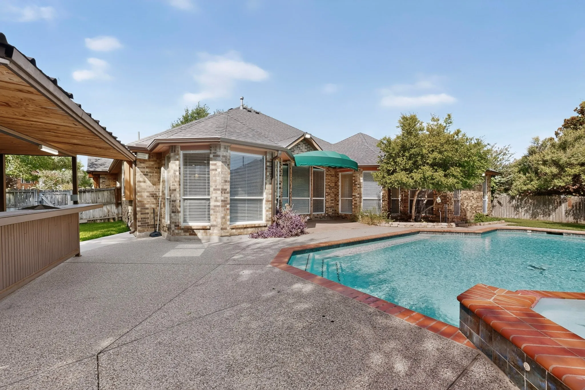 Pebble-finish concrete patio with a built-in bar, covered outdoor area, and a large swimming pool with a hot tub