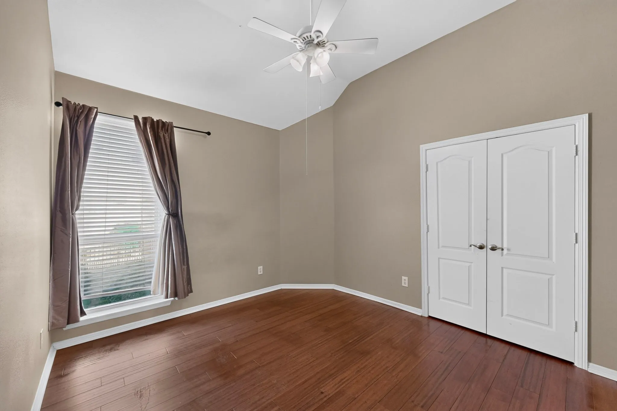 Vaulted ceiling, wood-finish flooring, ceiling fan, double doors, and window with blinds
