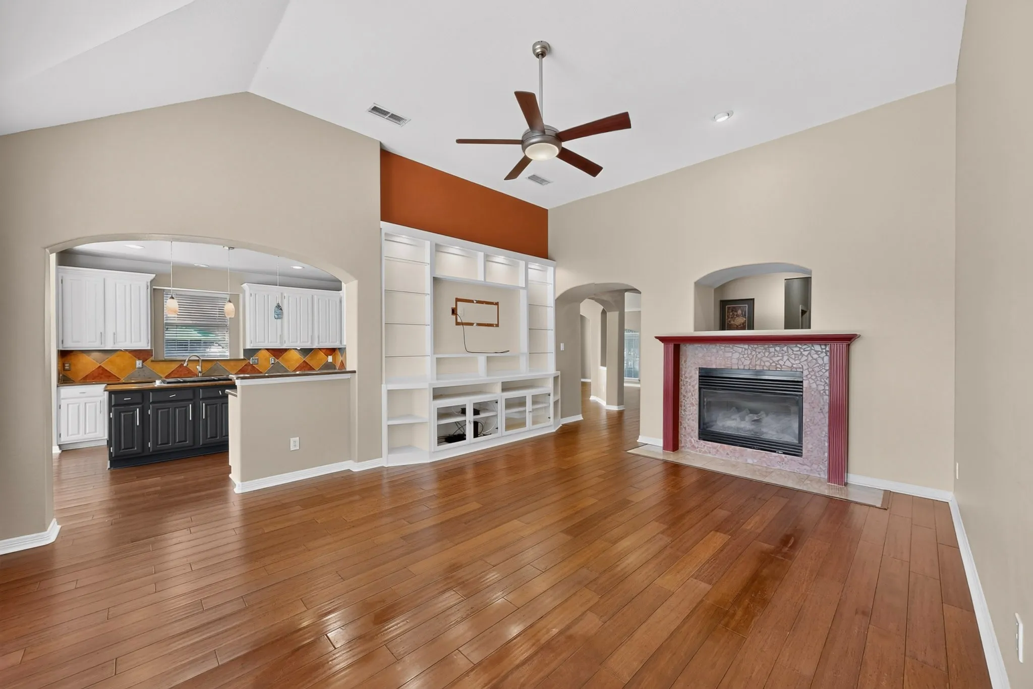 Wood-finish flooring, vaulted ceiling, built-in entertainment center, fireplace with tiled surround, and recessed lighting