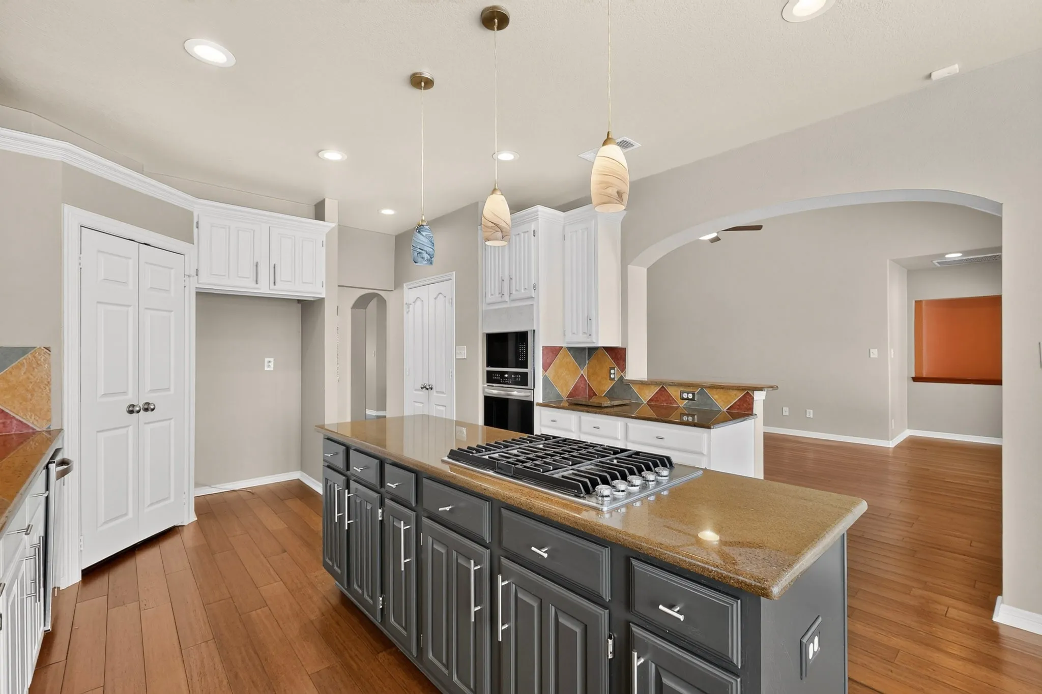Kitchen featuring a gas cooktop on a central island, recessed lighting, wood-finish flooring, and arched doorways