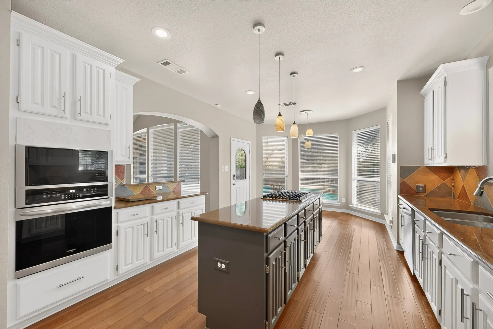 Kitchen featuring wood-finish flooring, white cabinetry, integrated stainless steel appliances, a center island with cooktop, and a bay window