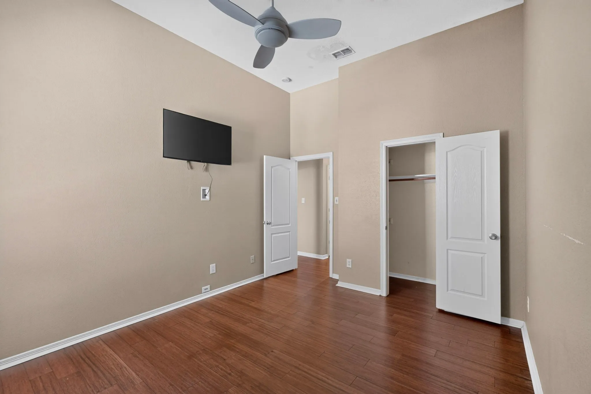 Wood-finish flooring, vaulted ceilings, ceiling fan, white interior doors, and built-in closet shelving