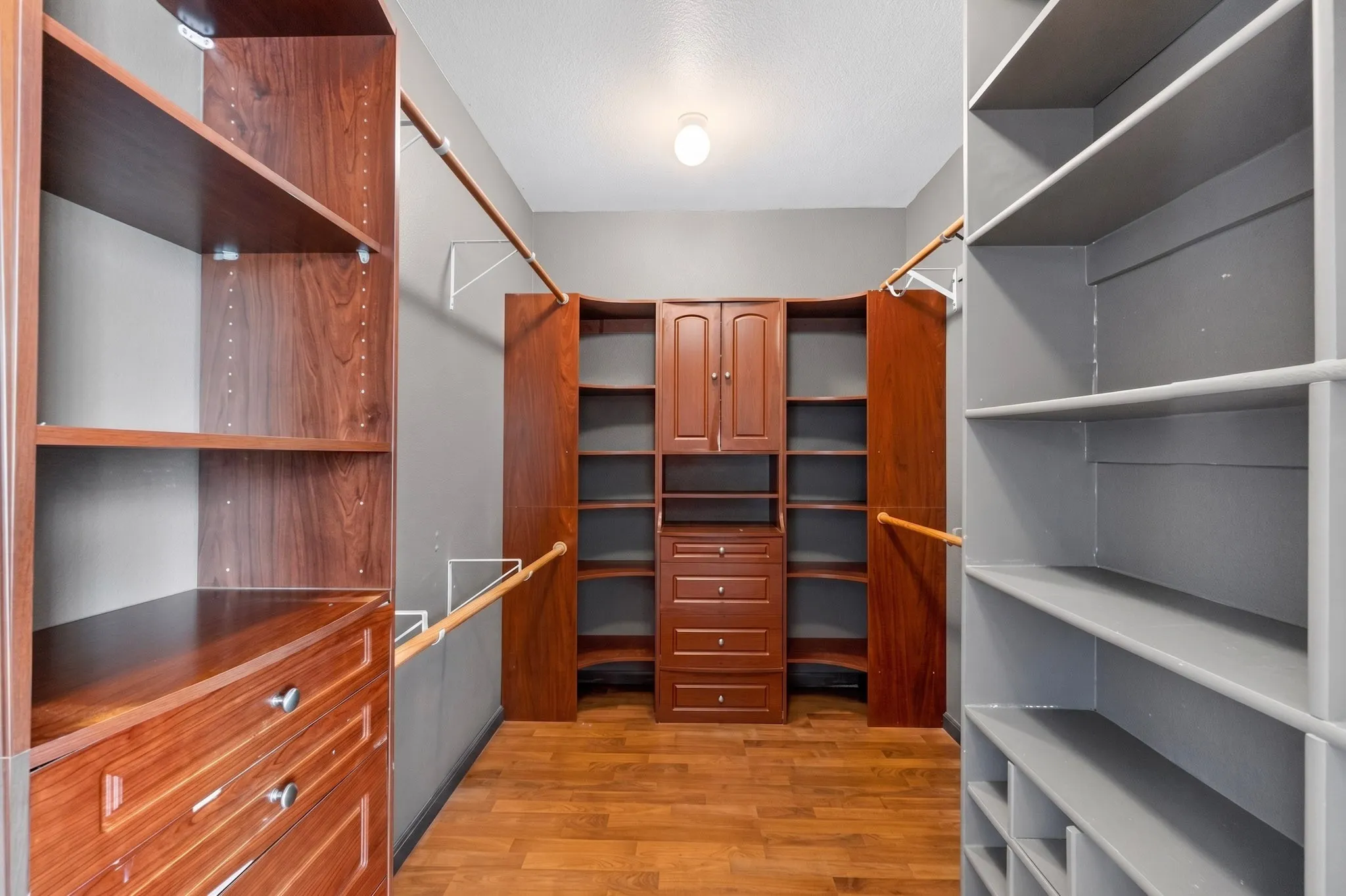Walk-in closet featuring wood-finish flooring, built-in shelving, integrated drawers, and hanging rods