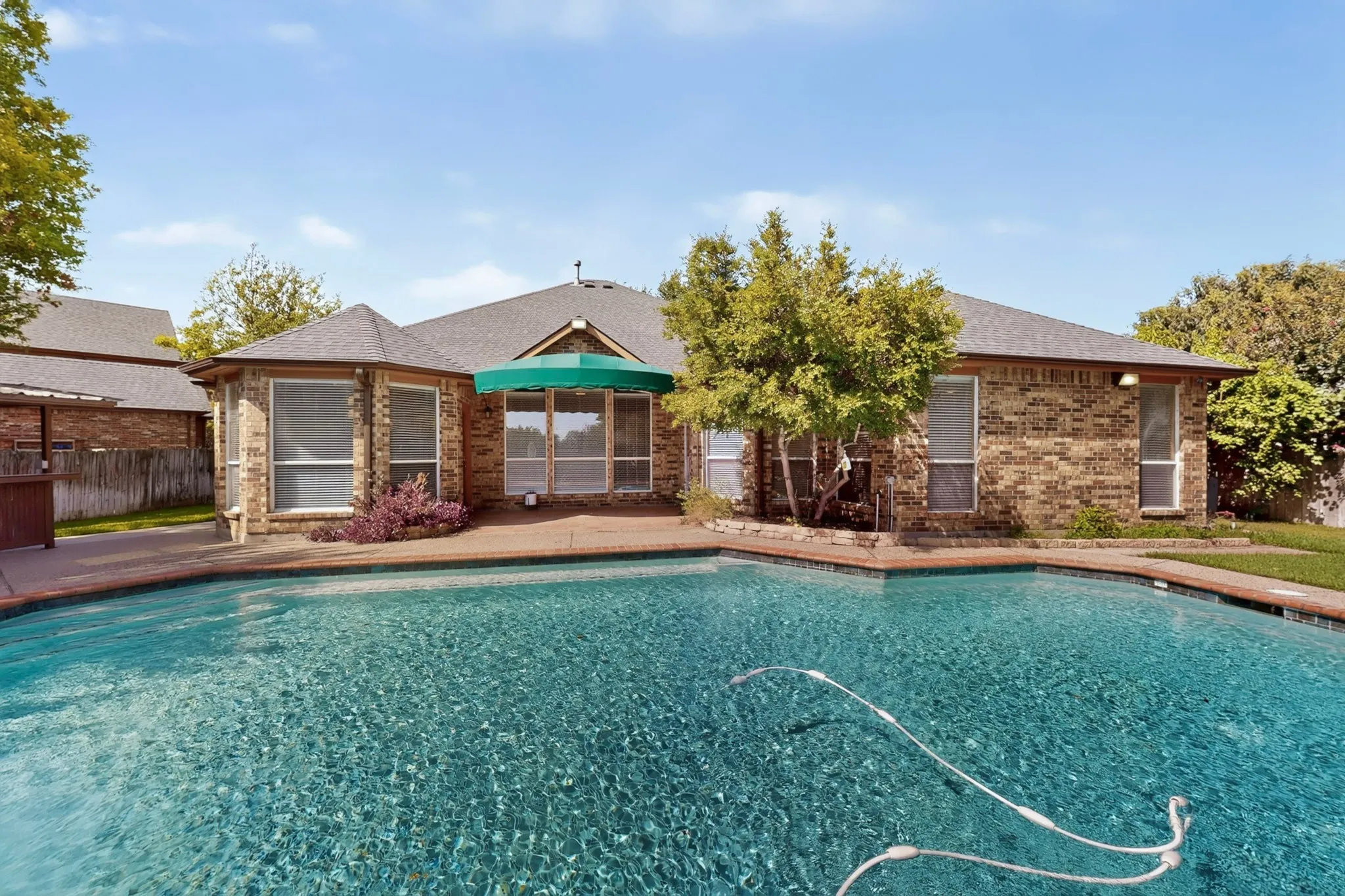 Expansive swimming pool with a concrete surround, brick exterior, multiple windows, and a green awning