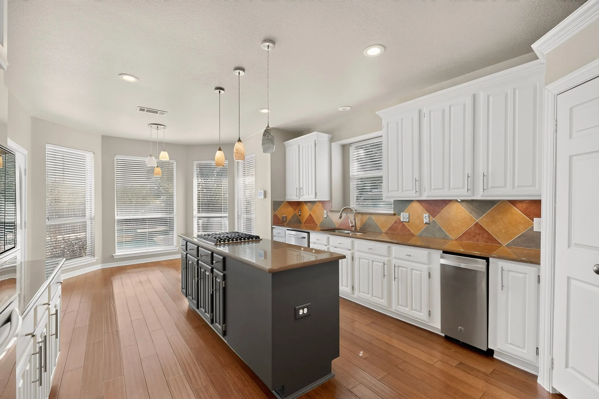 Kitchen featuring wood-finish flooring, white cabinetry, a tiled backsplash, and an island with an integrated cooktop and pendant lighting