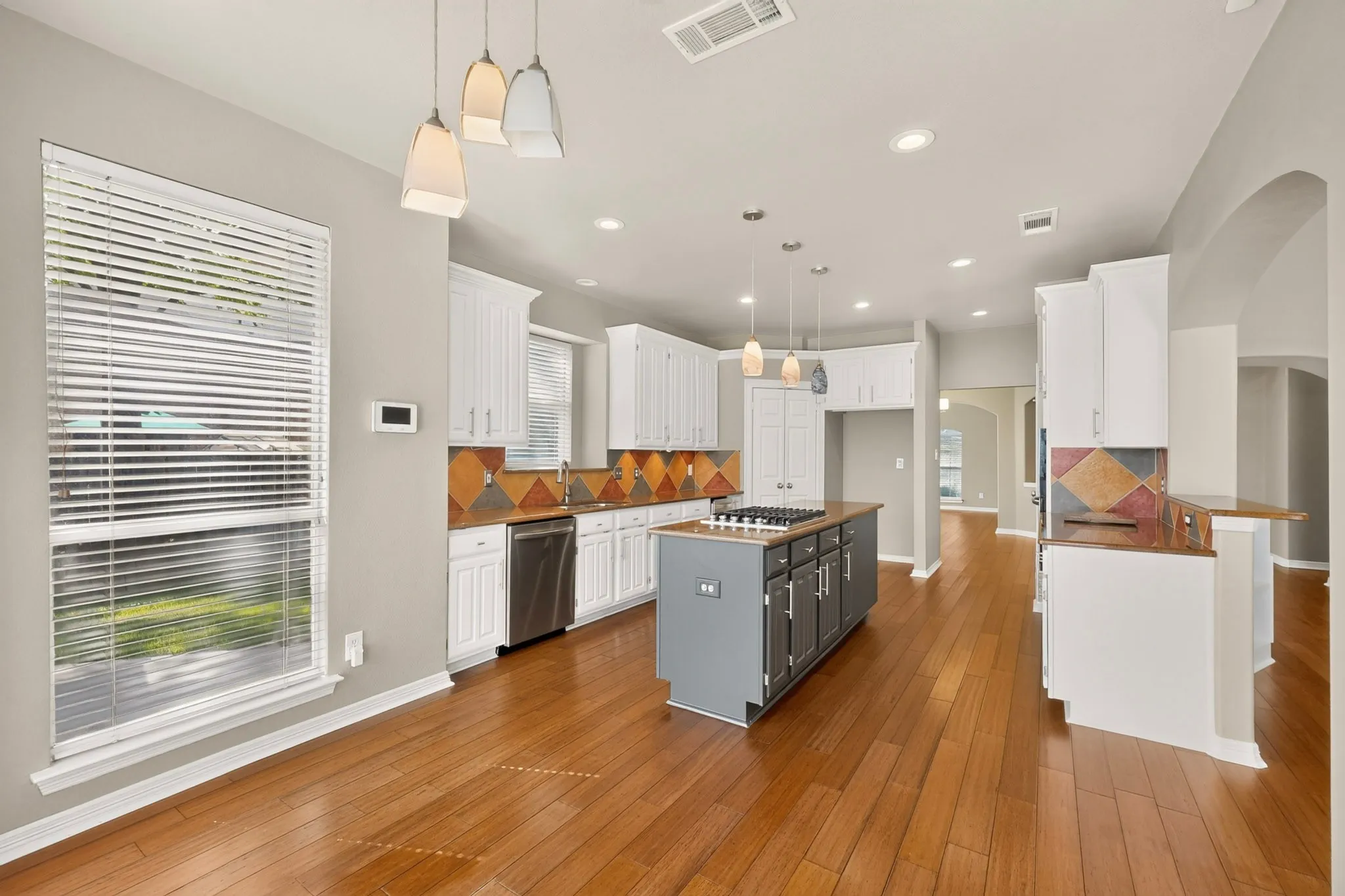 Kitchen featuring wood-finish flooring, white cabinetry, a center island with cooktop, stainless steel dishwasher, and recessed lighting