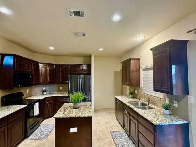 Kitchen with a sink, visible vents, black appliances, and dark brown cabinetry