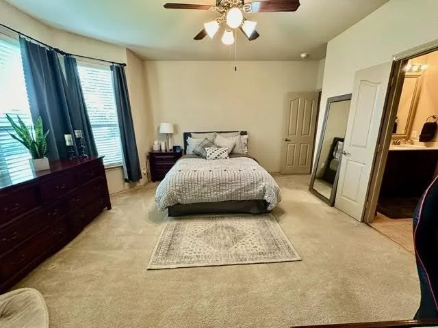 Bedroom with light carpet, connected bathroom, and a ceiling fan
