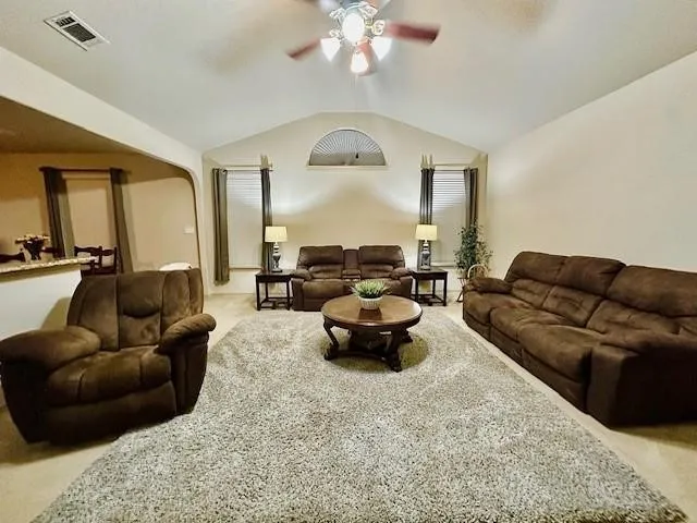 Living room featuring carpet floors, ceiling fan, visible vents, and vaulted ceiling