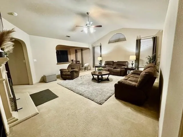 Carpeted living area with lofted ceiling, arched walkways, a fireplace, and a ceiling fan