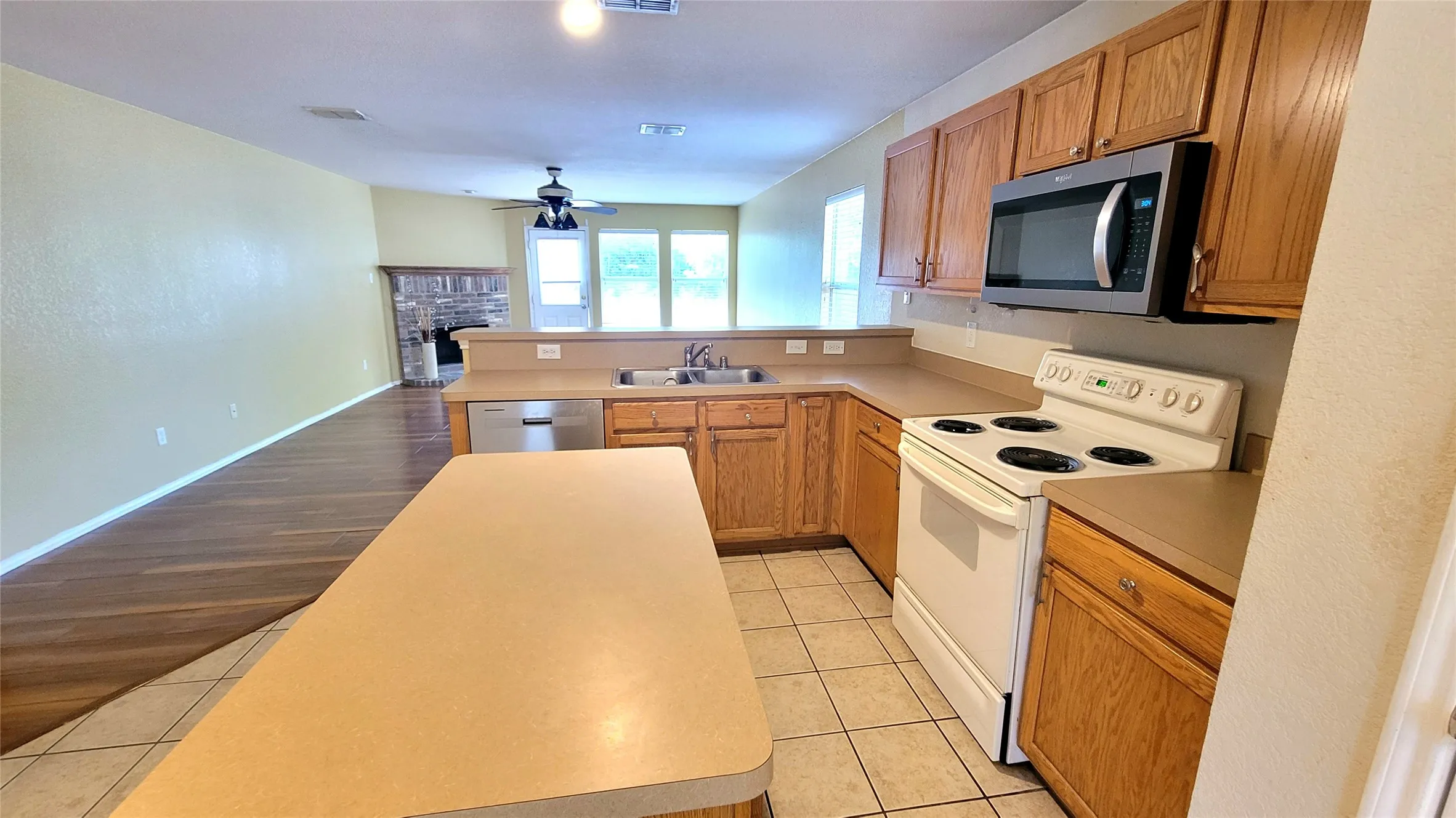 Kitchen featuring wood cabinetry, stainless steel microwave, white electric range, and light-toned countertops
