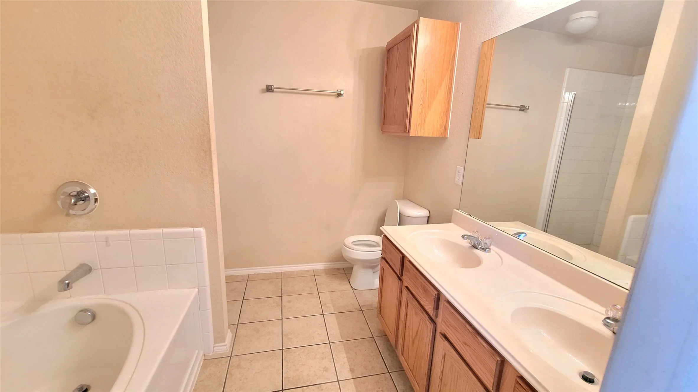 Bathroom featuring a double vanity, large mirror, wood-finish cabinetry, tile flooring, and a built-in bathtub with white tile surround