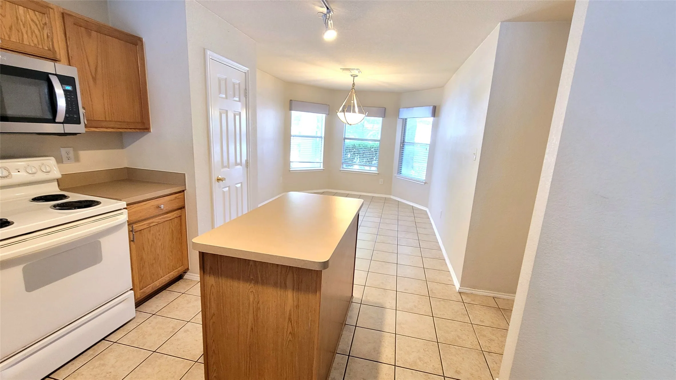 Kitchen island with counter seating, wood-finish cabinetry, tile flooring, built-in microwave, and an adjacent dining area with bay windows