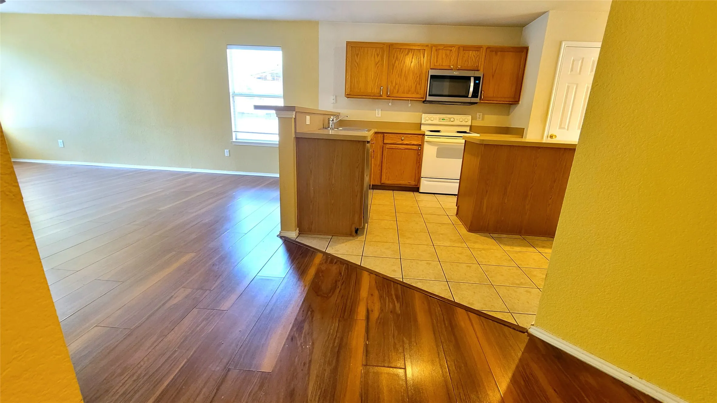 Wood-finish flooring and tile flooring, light wood cabinetry, white appliances, and a kitchen pass-through