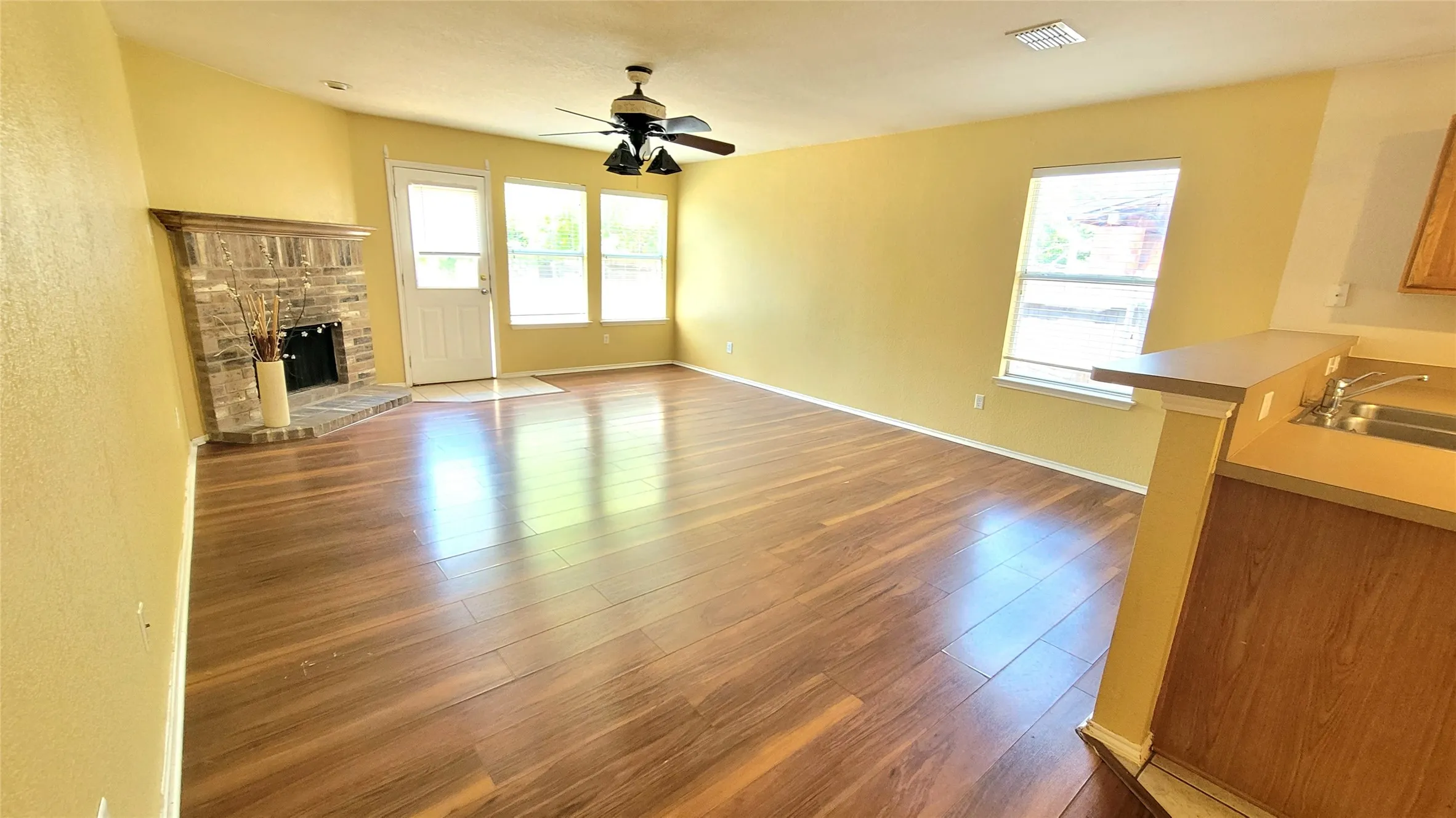 Spacious living area featuring wood-finish flooring, brick-surround fireplace, and an integrated ceiling fan