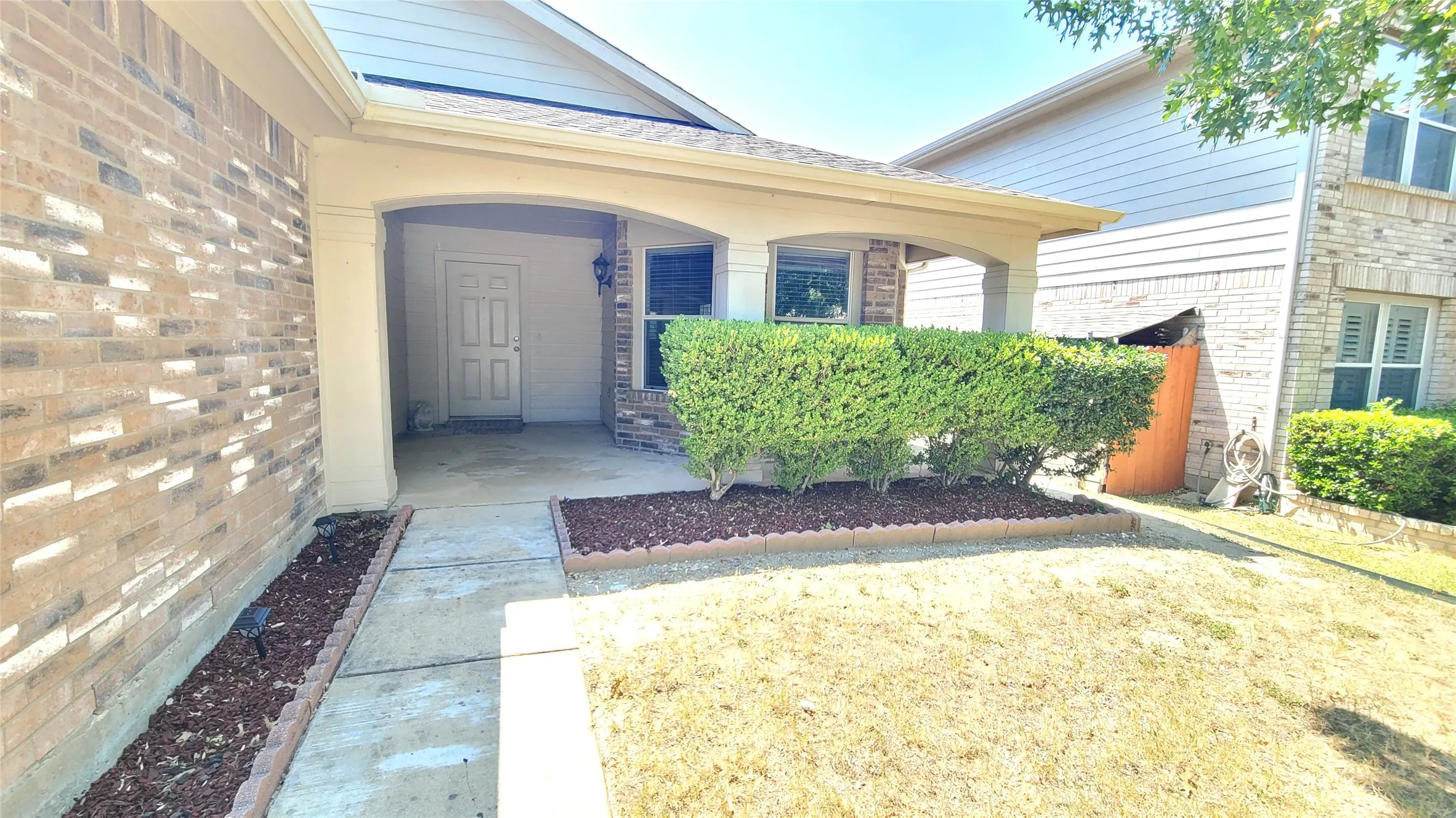 Brick facade with a covered entry, concrete walkway, and landscaped garden beds