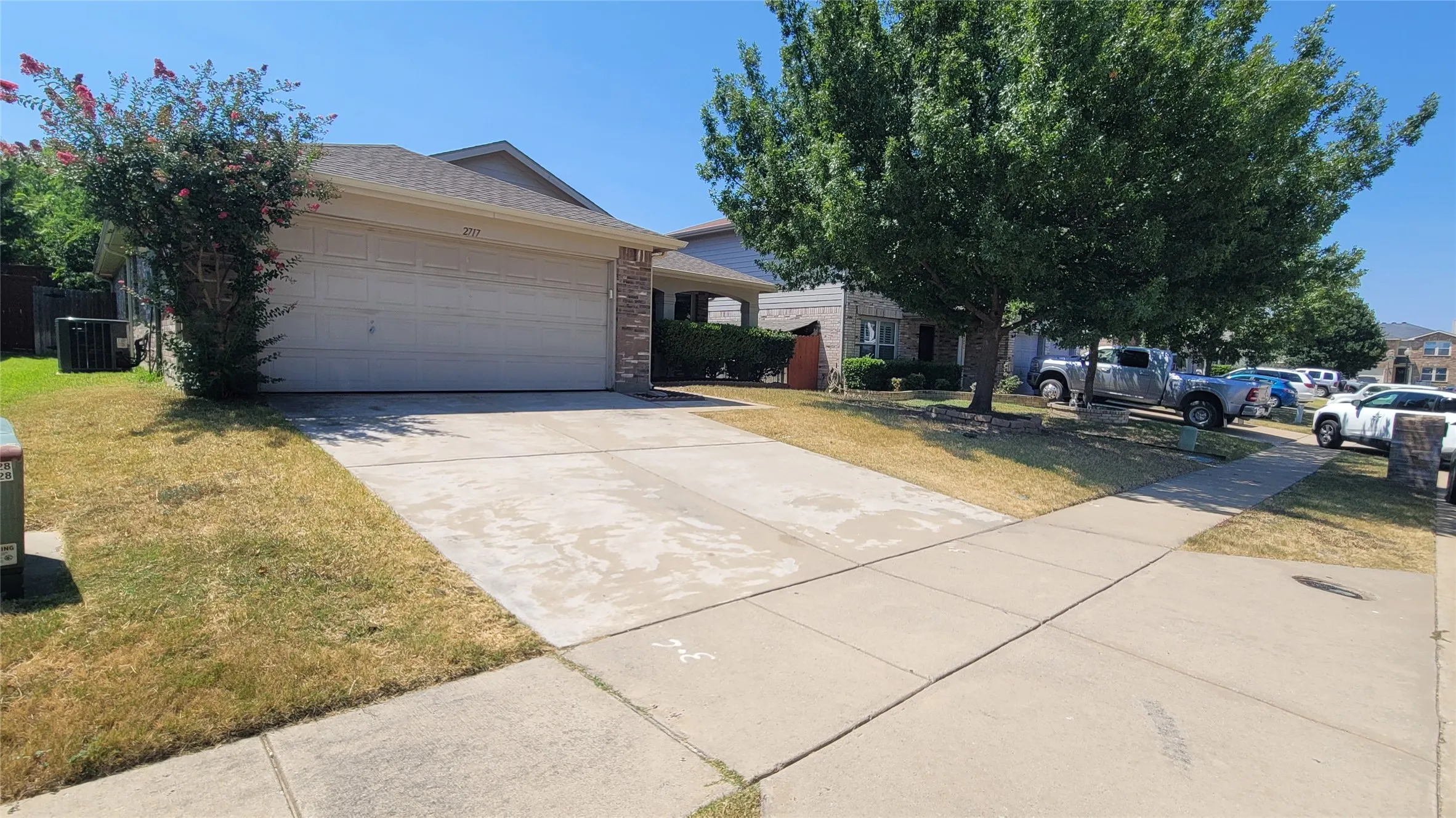 Two-car garage with a concrete driveway and sidewalk, featuring a mature shade tree and established landscaping