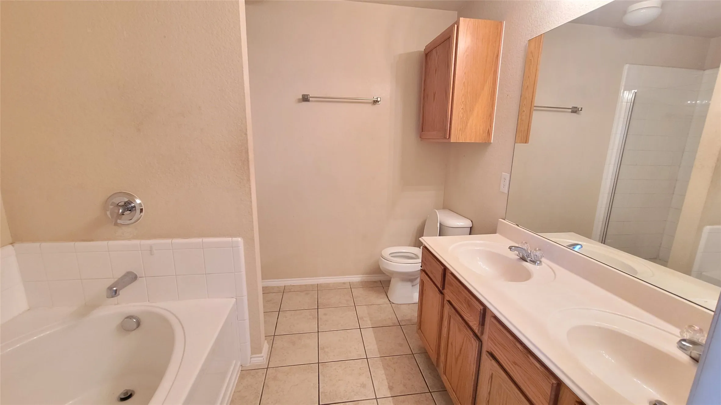 Double vanity with integrated sinks, wood-finish cabinetry, built-in bathtub with tiled surround, and ceramic tile flooring