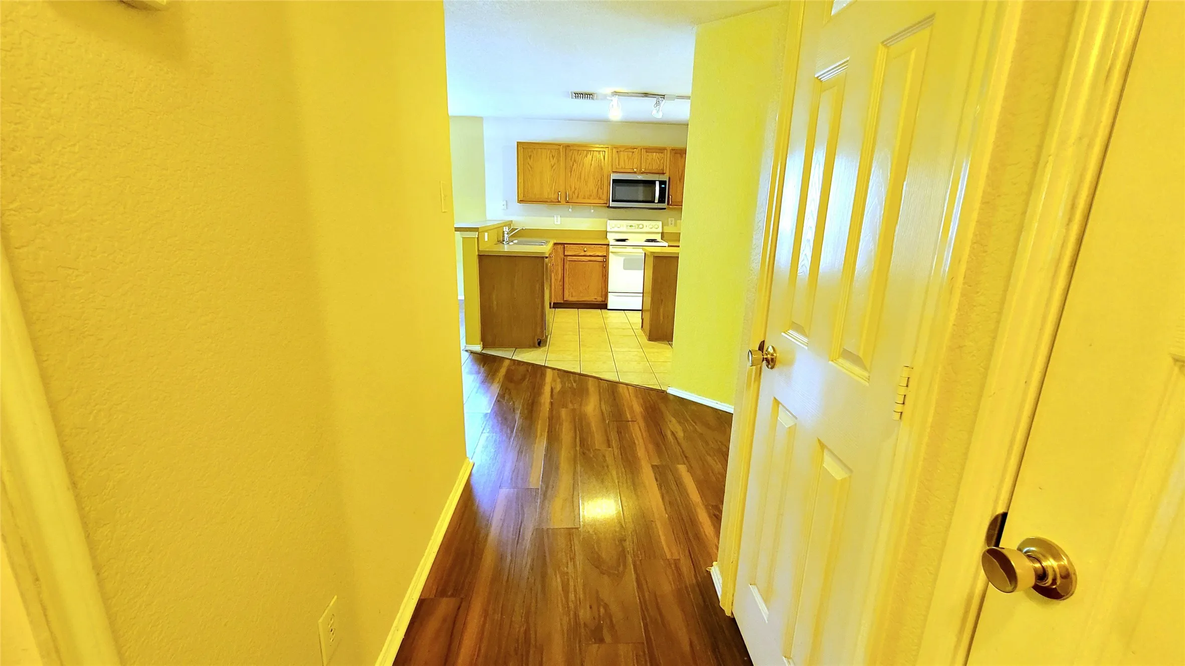 Wood-finish flooring, white paneled doors with brass hardware, and a kitchen featuring wood cabinetry, a microwave, and a range