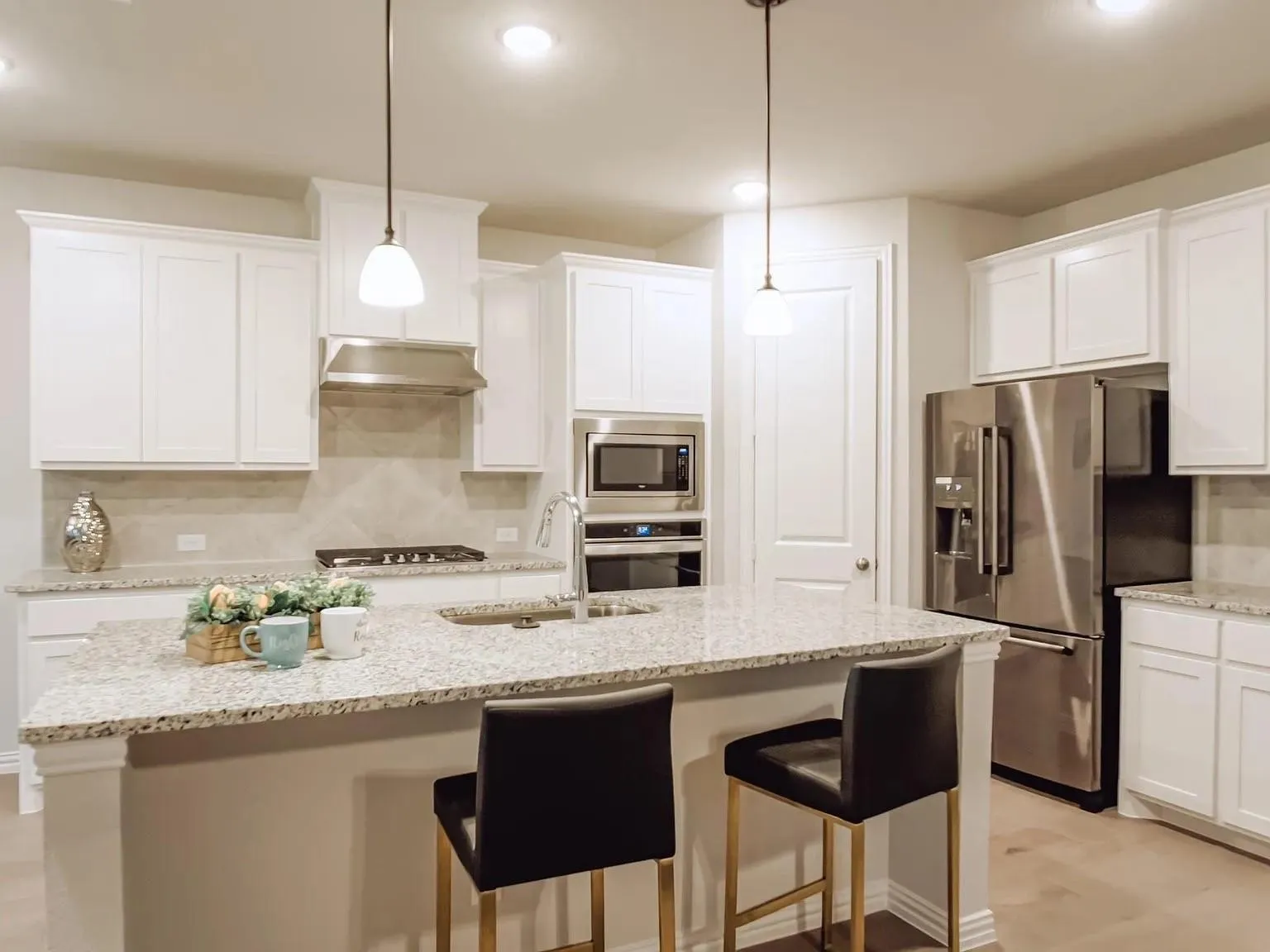 Kitchen with white cabinetry, granite countertops, stainless steel appliances, and a central island with sink